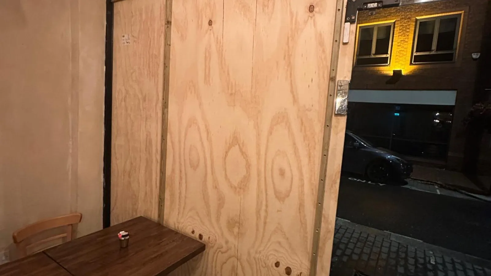 A glass shopfront door boarded up with plywood the same evening as a break-in