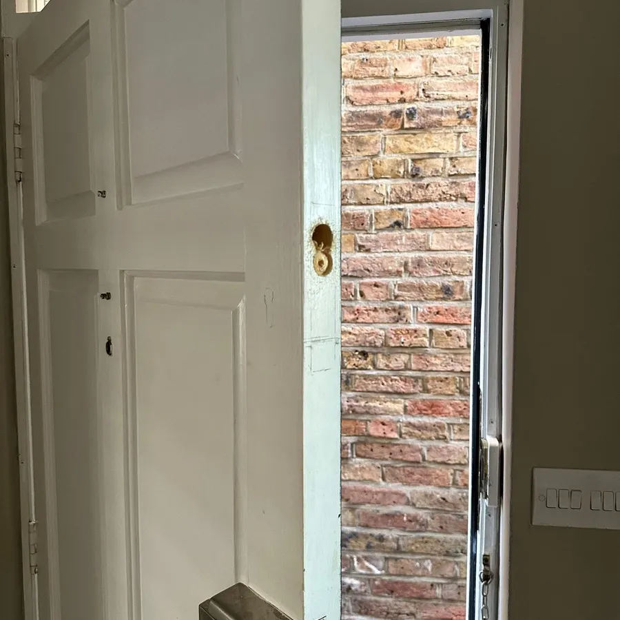 A front door mid-repair after forced entry, the damaged lock removed before the new one goes in