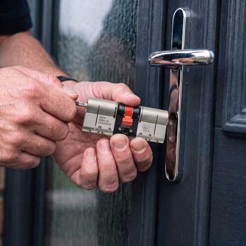 Hands fitting an anti-snap euro cylinder into a door in daylight.