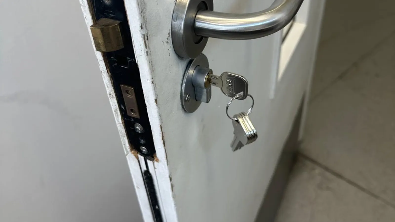 A staff door at business premises with the mortice latch exposed mid-repair, new handle and cylinder fitted